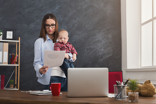 Blogbeitrag-Bild Junge Mutter mir Baby auf dem Arm arbeitet im Büro